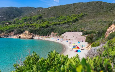 Una baia con acque cristalline e **spiagge** dell'Isola d'Elba, con ombrelloni colorati e gente che si rilassa sulla sabbia dorata.