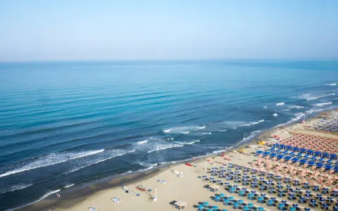 Ampia spiaggia libera al Lido di Camaiore, con file ordinate di ombrelloni e lettini che si estendono verso il mare azzurro.