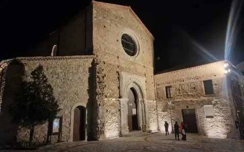 La chiesa di San Giovanni in Fiore illuminata di notte, con la sua facciata in pietra e il rosone circolare.