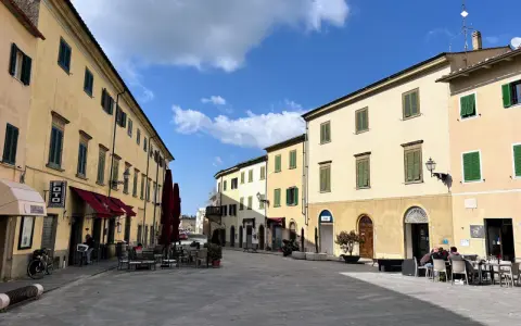 Piazza tranquilla a Pomarance, cosa vedere: edifici storici con persiane verdi, tavolini all'aperto di un bar.