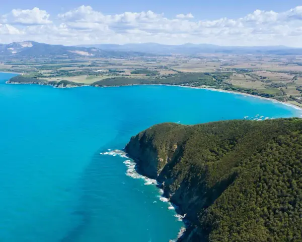 Vista aerea della costa degli Etruschi con mare azzurro, scogliere verdi e un borgo storico.