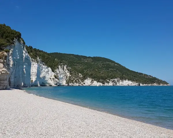 Scogliera bianca a picco sul mare turchese, con una spiaggia di ciottoli bianchi. Un angolo di paradiso, la spiaggia bianca Puglia.