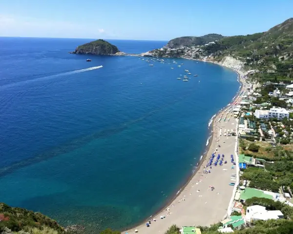 Vista panoramica della spiaggia dei Maronti, con il mare blu intenso, tante barche e la costa verdeggiante.