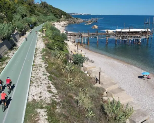 Ciclisti sulla pista ciclabile lungo mare, con i trabocchi che caratterizzano la costa dei Trabocchi cosa vedere. Spiaggia di ciottoli e mare azzurro.