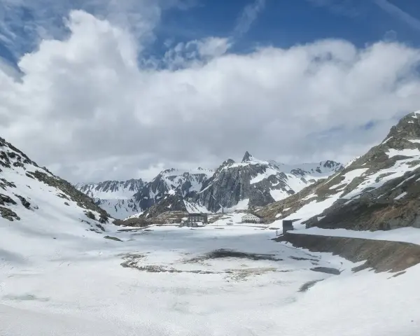 Paesaggio innevato al Gran San Bernardo con edifici storici e montagne maestose sotto un cielo nuvoloso.