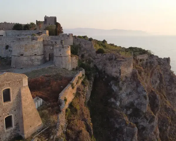 Il complesso monumentale del castello di Milazzo si erge su una scogliera a picco sul mare, con torri e mura antiche che dominano il paesaggio.
