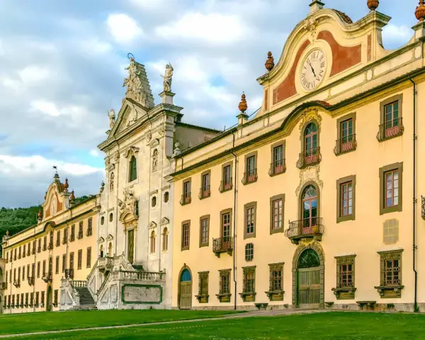 La maestosa Certosa di Calci, con la sua facciata imponente e il prato verde antistante, incanta sotto un cielo nuvoloso.