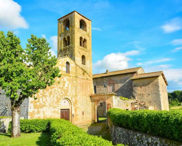 Antico campanile romanico e edifici in pietra nel **Sovicille centro storico**, con un albero verdeggiante e cielo azzurro.