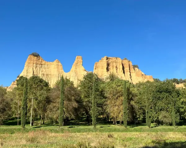 Le maestose balze del Valdarno si ergono sotto un cielo azzurro, circondate da una rigogliosa vegetazione e cipressi slanciati.