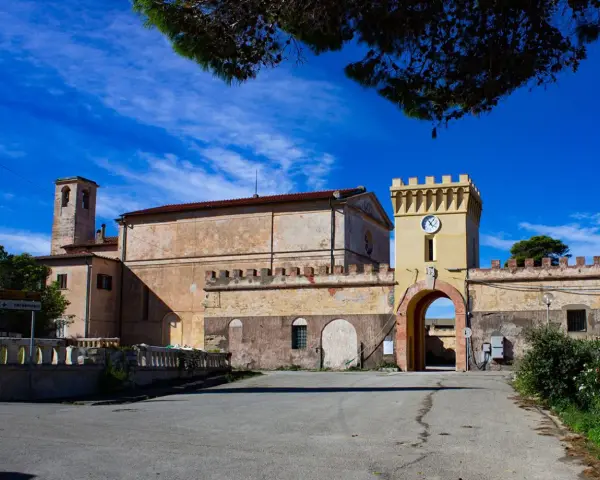 Antico borgo sull'isola di Pianosa, con torre dell'orologio e campanile sotto un cielo azzurro.