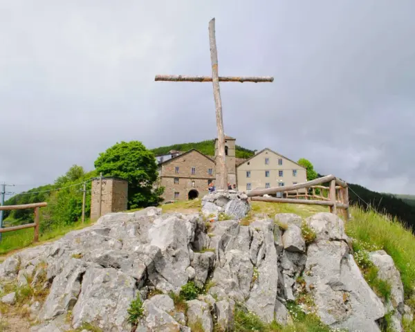 Croce di legno a San Pellegrino in Alpe, con edifici storici sullo sfondo e rocce in primo piano.