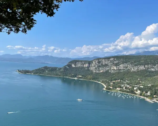Vista panoramica del Lago di Garda con San Zeno di Montagna sullo sfondo, tra montagne verdi e cielo azzurro.