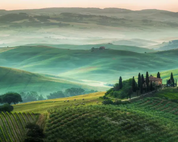 Dolci colline verdi del Val d'Orcia, con una casa colonica in cima a una collina e cipressi. Un paesaggio da cartolina, uno dei tanti punti panoramici mozzafiato.