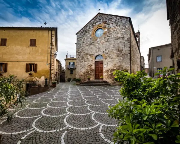 Piazza di Bibbona, cosa vedere: chiesa in pietra con rosone, case gialle e pavimentazione a ventaglio.