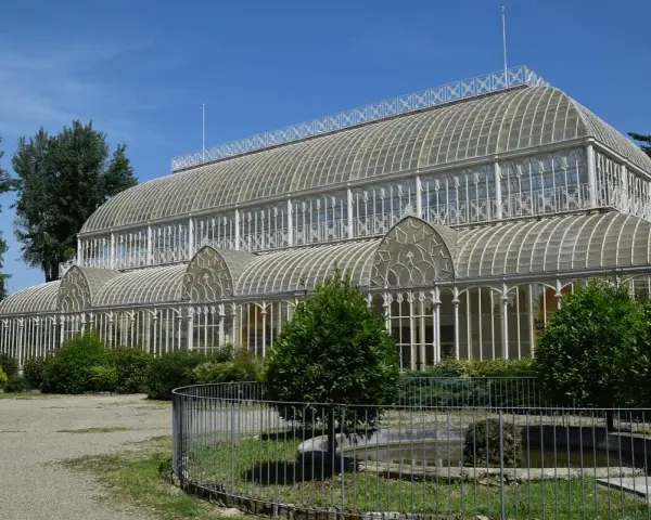 Serra in vetro con archi decorati, parte del giardino orticoltura firenze, circondata da alberi e vegetazione.