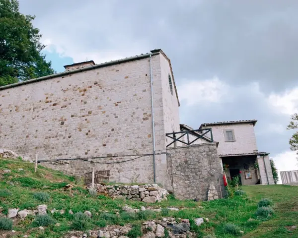 Antico eremo di Cerbaiolo, con muri in pietra grezza e vegetazione rigogliosa che sale sul pendio.