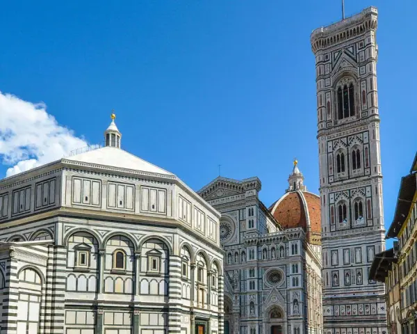 La piazza del Duomo a Firenze con il Battistero, il Campanile di Giotto e la cupola del Brunelleschi sotto un cielo azzurro.