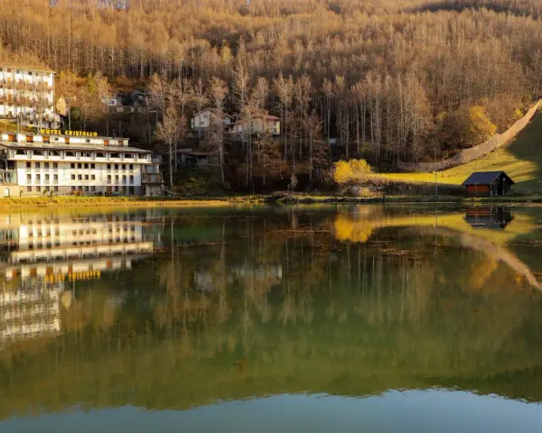 Hotel Cristallo sul Passo del Cerreto, riflesso sull'acqua calma di un lago circondato da boschi autunnali.