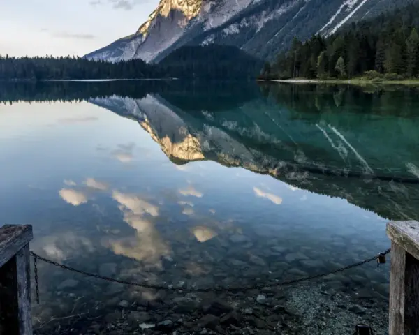 Lago alpino con riflessi di montagne e nuvole, un pontile in legno invita a contemplare la bellezza del Val di Non.