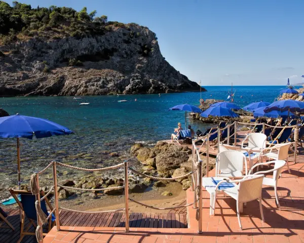 Le argentario spiagge più belle, con ombrelloni blu e lettini su una terrazza in legno, affacciate sul mare cristallino.