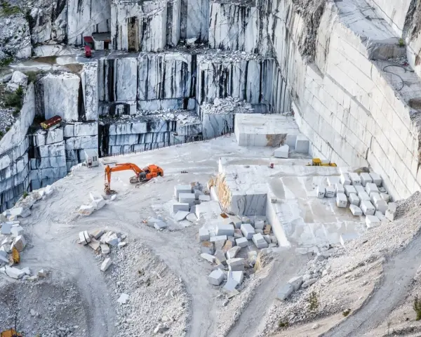 Cava di marmo a Carrara, con escavatore arancione al lavoro tra blocchi di pietra bianca. Un luogo affascinante da vedere a Carrara.