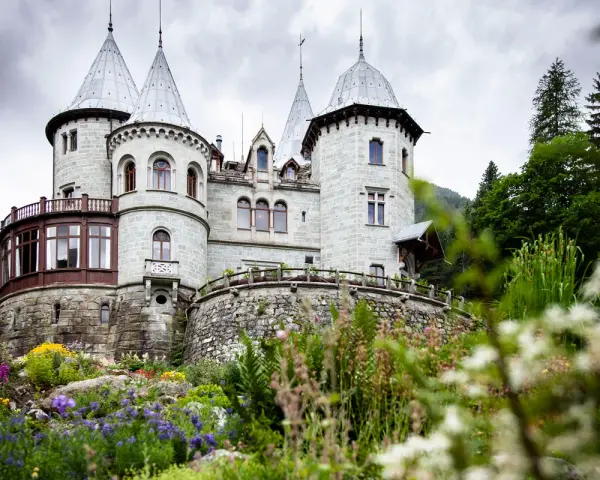 Un fiabesco castello in pietra, tra i castelli Val d'Aosta, circondato da un giardino fiorito e boschi rigogliosi.