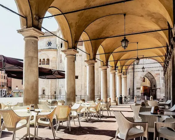 Tavolini all'aperto sotto un portico con vista sul Duomo. Un'idea su cosa fare a Modena: godersi un caffè in piazza.