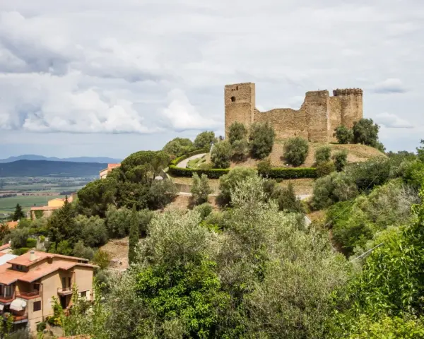 Rovine di un castello dominano il **Scarlino centro storico**, circondato da ulivi e case con tetti rossi.