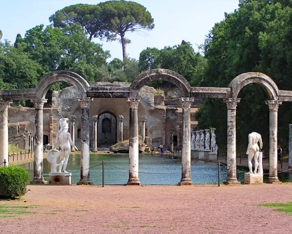 Resti archeologici di Villa Adriana con statue classiche e un laghetto, immersi nel verde.