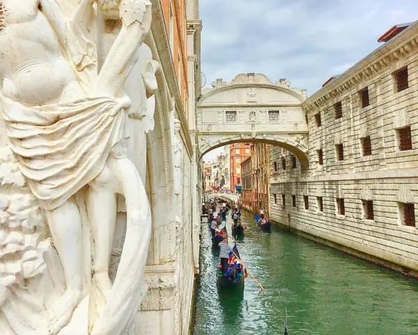 Gondole scivolano sul canale sotto il Ponte dei Sospiri, con un'imponente statua in primo piano.