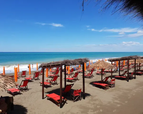 Spiaggia attrezzata a Marina di Bibbona, con lettini rossi, ombrelloni di paglia e il mare azzurro all'orizzonte.