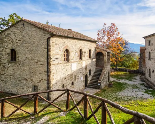 Antica strada in Casentino conduce a un borgo in pietra con un cortile interno e un albero dalle foglie arancioni.