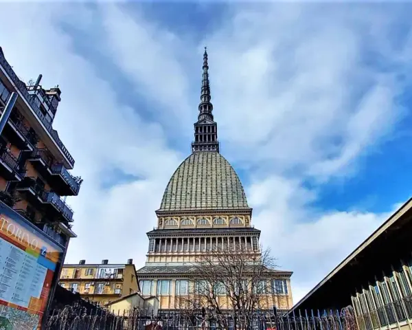 La Mole Antonelliana svetta maestosa nel cielo azzurro di Torino, circondata da edifici moderni e storici.