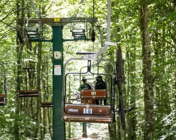 La funivia Monte Amiata trasporta due persone e una mountain bike tra gli alberi rigogliosi.