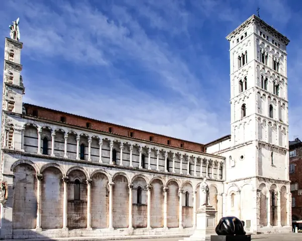 La piazza San Michele a Lucca, con la sua chiesa romanica e la torre campanaria imponente, sotto un cielo azzurro.