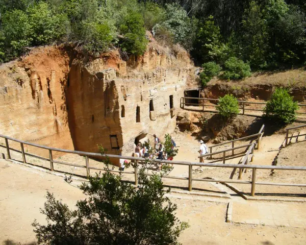 Antiche cave di tufo scavate nella roccia, con finestre e ingressi. Un gruppo di turisti esplora questo luogo affascinante, tra i **baratti cosa vedere** e la natura rigogliosa.