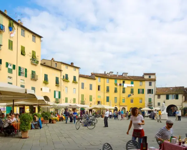 Passeggiata nella storica piazza anfiteatro di Lucca, con i suoi palazzi gialli e i tavolini all'aperto.