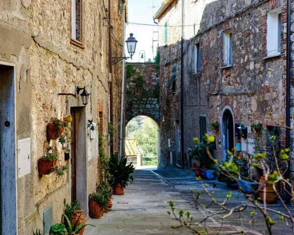 Un vicolo suggestivo a Monteverdi Marittimo, con case in pietra, piante in vaso e un arco che si apre su un paesaggio verde.