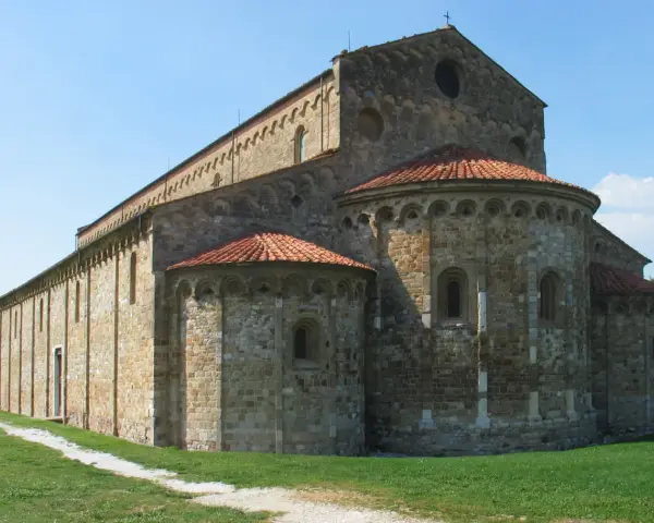 Antica basilica romanica di San Piero a Grado, con absidi semicircolari e tetto in cotto, immersa nel verde.