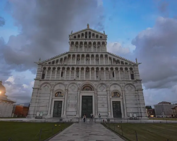 La maestosa **cathédrale de Pise** si erge sotto un cielo nuvoloso, con la sua facciata ricca di arcate e decorazioni.