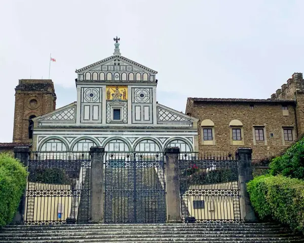 La facciata marmorea di San Miniato al Monte domina la vista, con un cancello in ferro battuto che precede la scalinata.