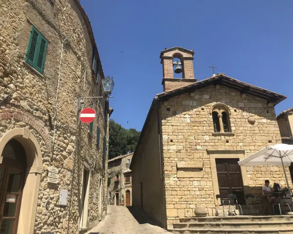 Un vicolo a Casale Marittimo, Pisa, con edifici in pietra, una chiesa con campanile e un tavolino all'aperto.