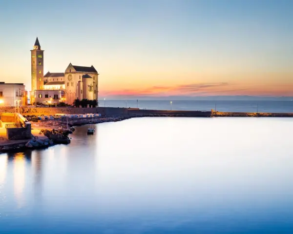 La cattedrale di Trani si erge maestosa sul mare al tramonto, illuminata da luci calde.