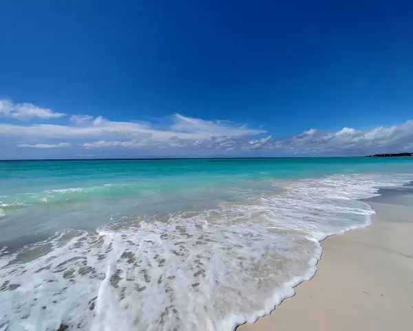 Onde turchesi lambiscono le spiagge bianche di Marina di Cecina, sotto un cielo azzurro con nuvole sparse.