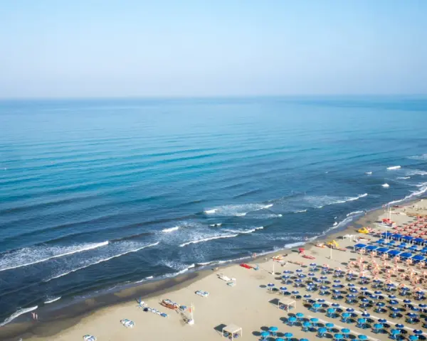 Ampia spiaggia libera al Lido di Camaiore, con file ordinate di ombrelloni e lettini che si estendono verso il mare azzurro.