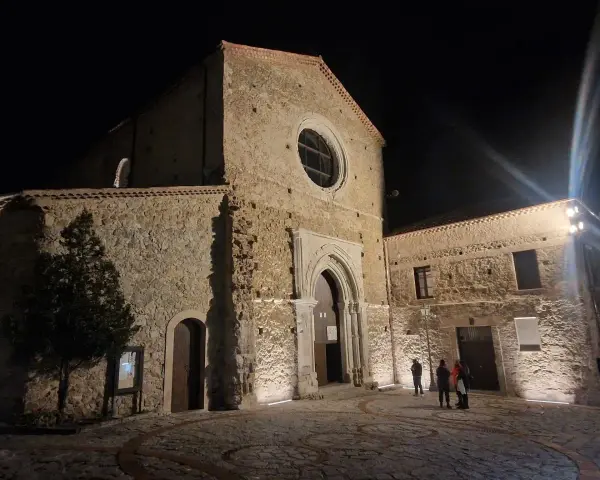 La chiesa di San Giovanni in Fiore illuminata di notte, con la sua facciata in pietra e il rosone circolare.
