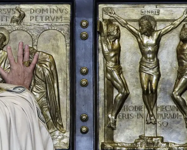 Mano che tocca la porta santa San Pietro, con scene della crocifissione e del rinnegamento di Pietro.