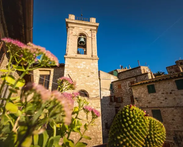 Campanile in pietra in un borgo delle Colline Metallifere, con fiori rosa in primo piano e cielo azzurro.