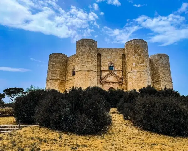 Castel del Monte, un'icona pugliese, si erge maestoso su una collina, circondato da una vegetazione rigogliosa sotto un cielo azzurro.