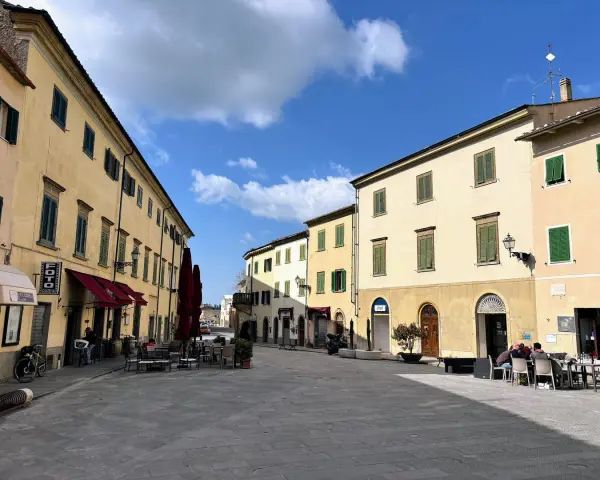 Piazza tranquilla a Pomarance, cosa vedere: edifici storici con persiane verdi, tavolini all'aperto di un bar.
